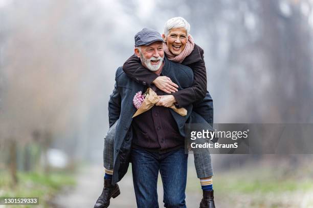 giocoso piggybacking di coppia maturo nella giornata invernale. - pensionamento foto e immagini stock