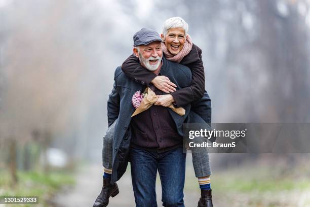 playful mature couple piggybacking in winter day. - jovem de espírito imagens e fotografias de stock