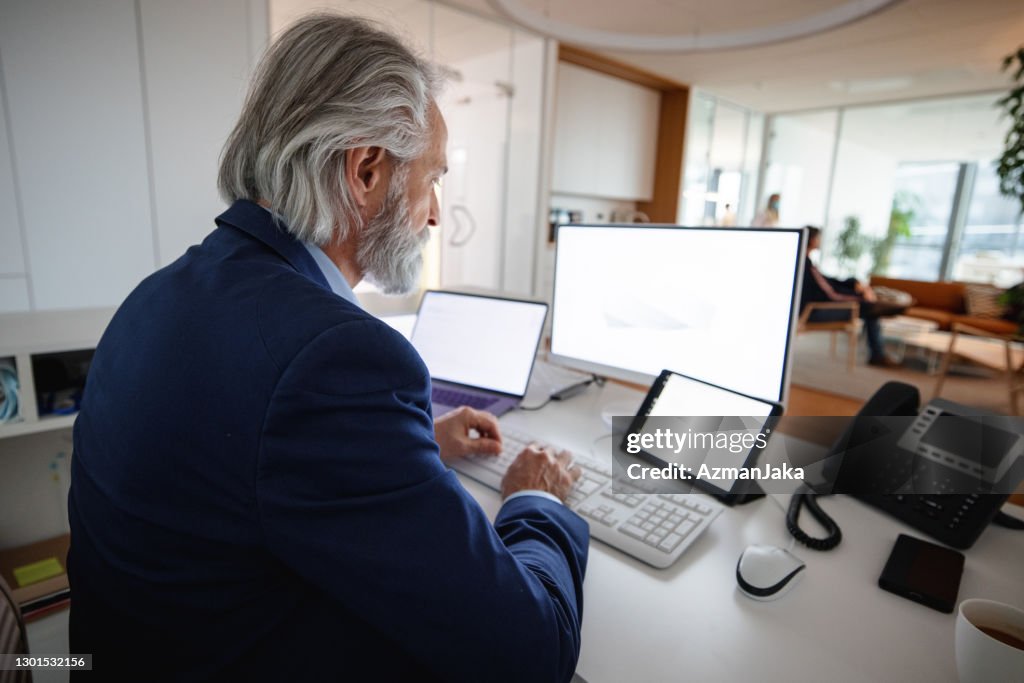 Businessman analyzing data while looking at multiple computer screens in office