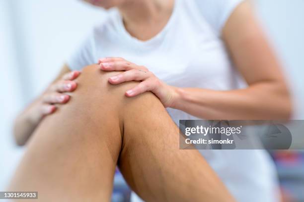 female physiotherapist massaging patient's knee - standing with hands on knees imagens e fotografias de stock