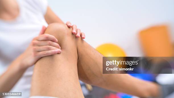 fisioterapeuta femenina masajeando la rodilla del paciente - knees together fotografías e imágenes de stock