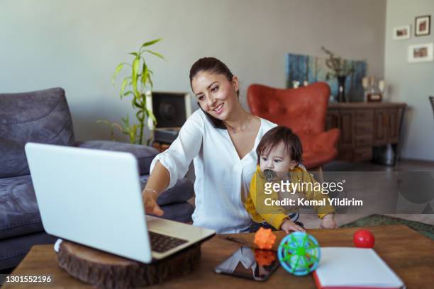 joven bonita mamá trabajando desde casa mientras cuida de su bebé niño - family politics fotografías e imágenes de stock