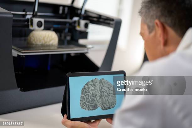 male biomedical engineer holding digital tablet while standing next to 3d printer - organe de reproduction masculin imagens e fotografias de stock
