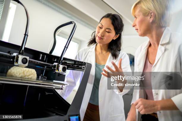 mujeres ingenieras biomédicas de pie junto a la impresora 3d y discutiendo el proceso - invento fotografías e imágenes de stock