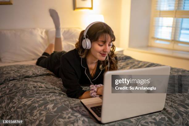 jong meisje dat laptop met hoofdtelefoons in haar bed gebruikt - girl in her bed stockfoto's en -beelden