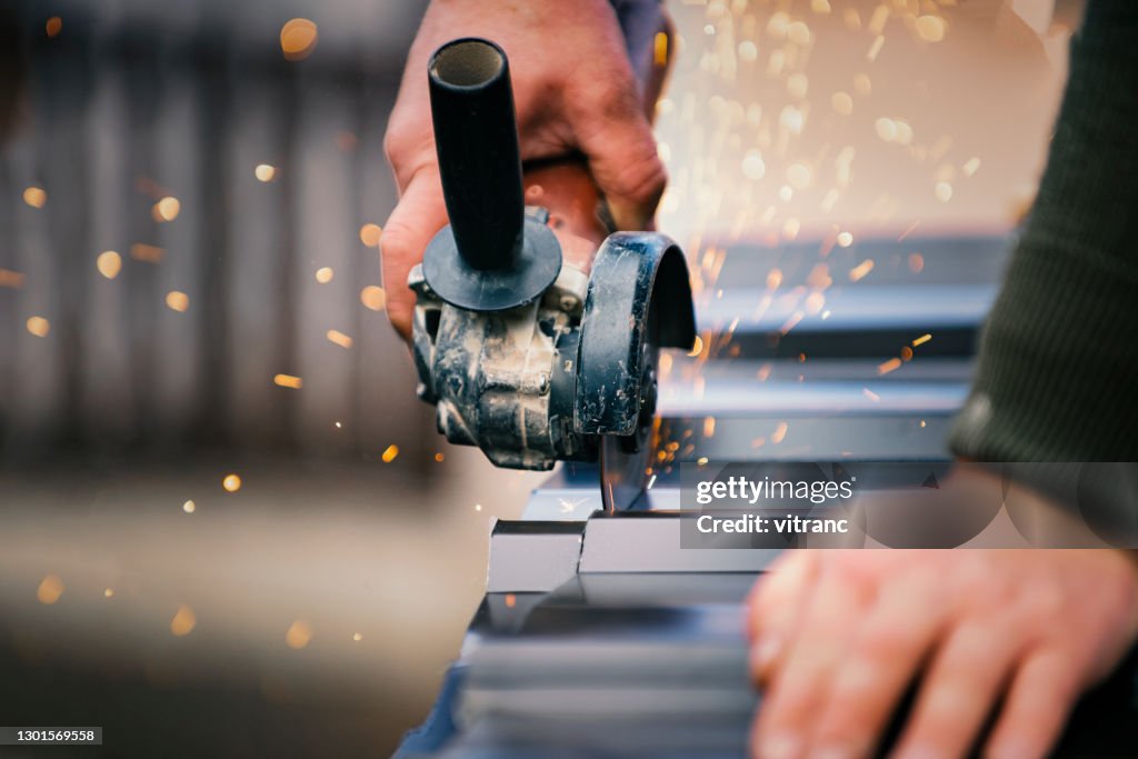 Building contractor is cutting lightweight metal, steel, corrugated, paint coated roofing sheet with an electric angle grinder