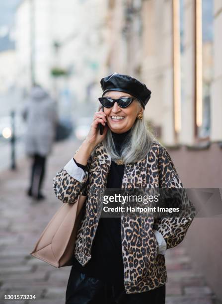 senior woman with extravagant clothes walking outdoors in town. - cat with red hat fotografías e imágenes de stock