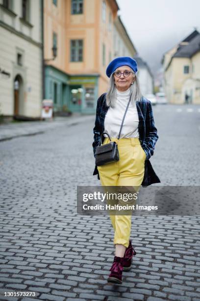 portrait of senior woman with blue beret walking outdoors in town. - man portrait full body 50's stock-fotos und bilder