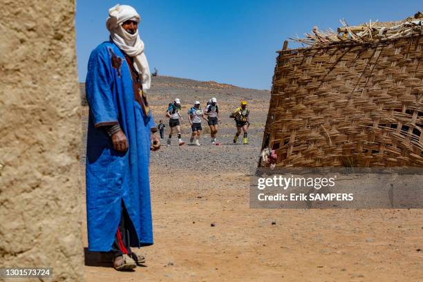 Homme marocain en djellaba et coureurs lors du Marathon des Sables, 7 avril 2019, Maroc.