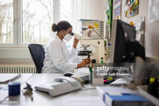 scientist in the lab using microscope - n95 face mask medical stock pictures, royalty-free photos & images