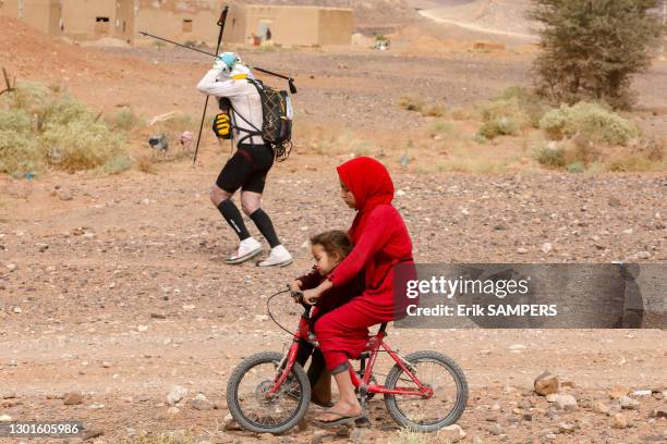 Le coureur français Benoit Pelier et fillette en robe rouge sur un vélo avec sa petite soeur lors du Marathon des Sables, 10 avril 2019, Maroc.