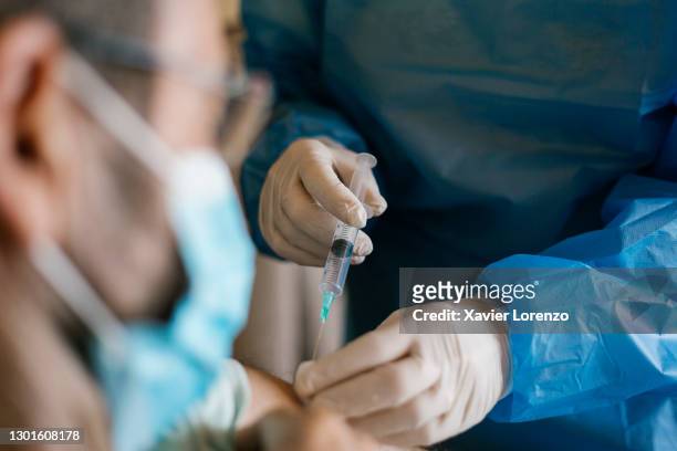 doctor injecting covid-19 vaccine to senior man at his home. - covid 19 vaccine stock pictures, royalty-free photos & images