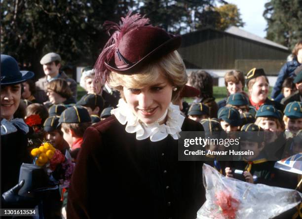 Diana, Princess of Wales, wearing a maroon velvet suit designed by Jaeger and a matching hat with an Ostrich plume designed by John Boyd, is greeted...