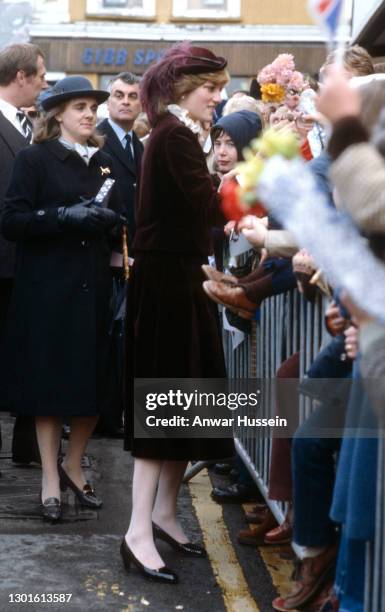 Diana, Princess of Wales, wearing a maroon velvet suit designed by Jaeger and a matching hat with an Ostrich plume designed by John Boyd, is greeted...