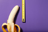 Yellow banana penis concept measured by measuring tape on a purple background.