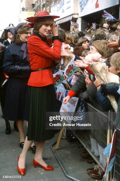 Diana, Princess of Wales, wearing a red suit with a black pleated skirt designed by Donald Campbell and a hat designed by John Boyd, is greeted by...