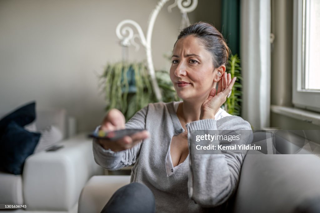 Ung vuxen kvinna med hörapparat tittar på TV