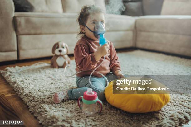 the girl holds the mask from the inhaler by herself and inhales in the living room - cystic fibrosis 個照片及圖片檔