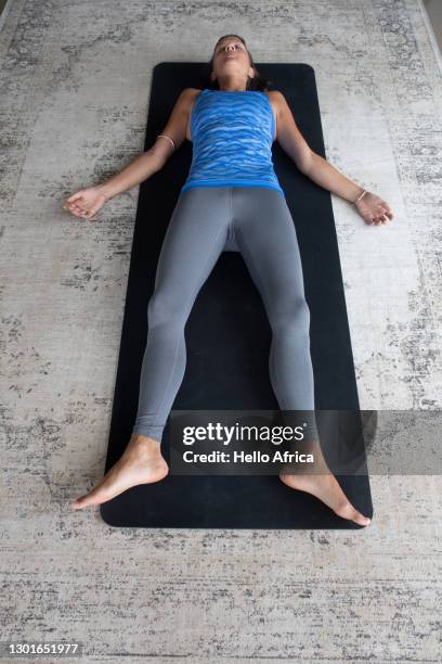 woman laying down on her mat in shavasana hatha yoga pose - savasana stock pictures, royalty-free photos & images