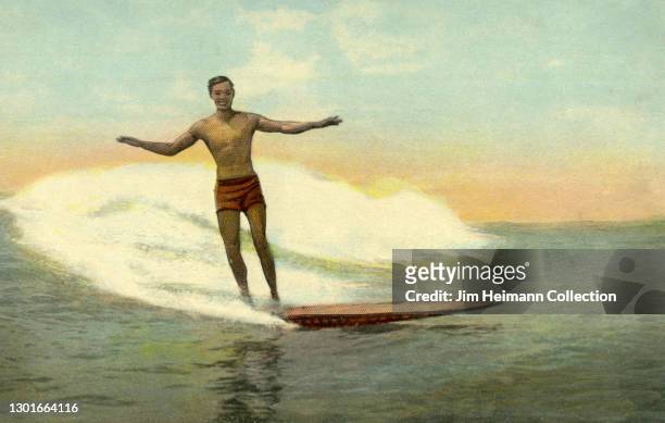Souvenir postcard shows a man riding a wave on a surfboard with his arms outstretched and a big grin, circa 1910.