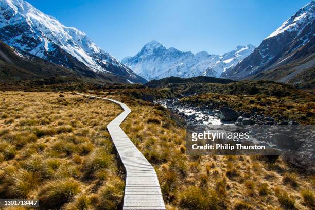 mountain footpath boardwalk in valley surrounded by snowcapped mountains - new zealand stock pictures, royalty-free photos & images
