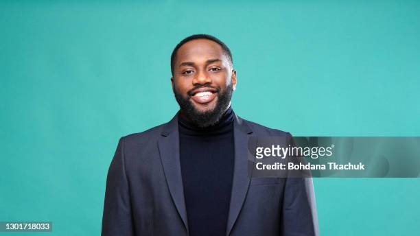oprechte afro amerikaanse mens in jasje glimlacht rakende borst - studio shot stockfoto's en -beelden
