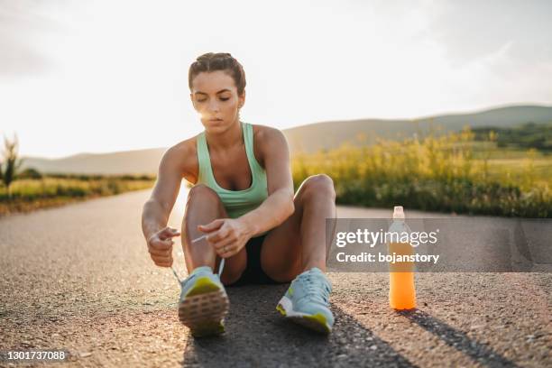 female runner tying her shoes preparing for a jog - energy drink stock pictures, royalty-free photos & images