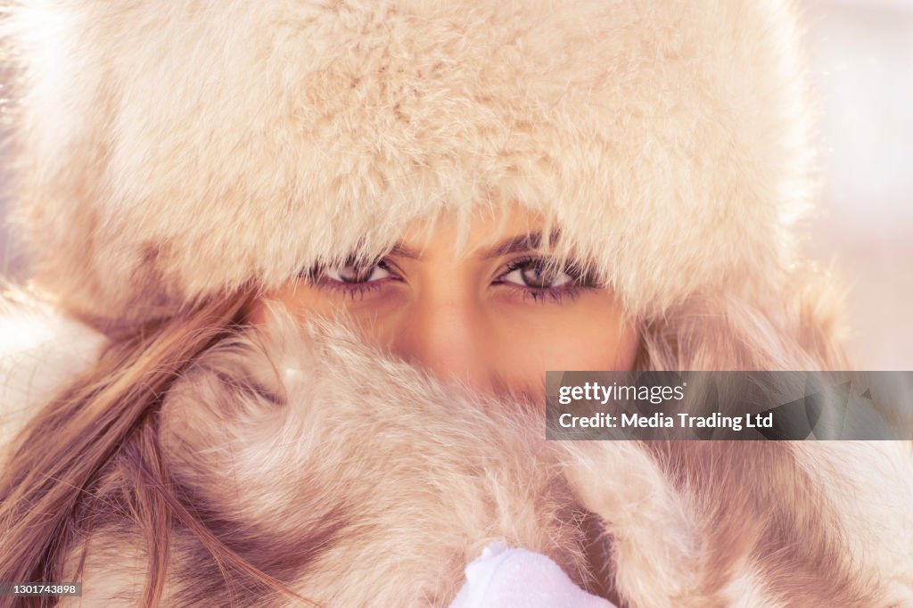 Mooie vrouw met bonthoed die camera in het winterpark in de stad tijdens de dag in sneeuwweer met dalende sneeuw, close-up bekijkt