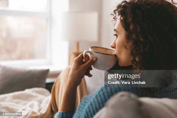 cup of tea and chill. woman lying on couch, drinking hot coffee and enjoying morning, being in dreamy and relaxed mood. girl in oversized shirt takes break at home. - kaffee getränk stock-fotos und bilder