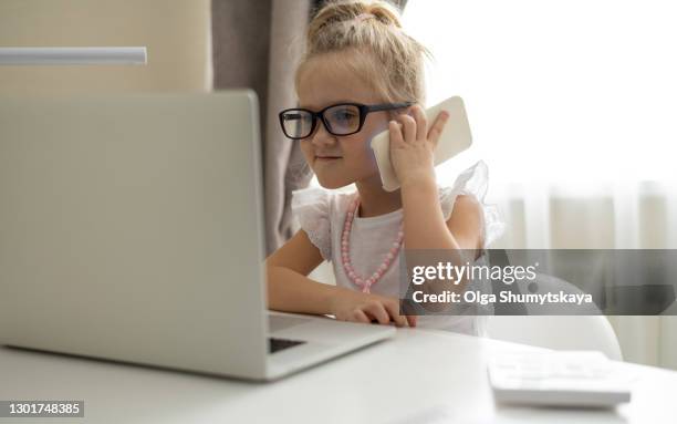 girl child speaks on phone using computer on home schooling - kid chef stock-fotos und bilder