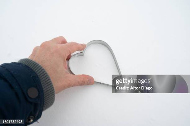 a person (man) makes the shape of a heart in the snow with a metal heart-shaped template. - frostbite fingers stock pictures, royalty-free photos & images