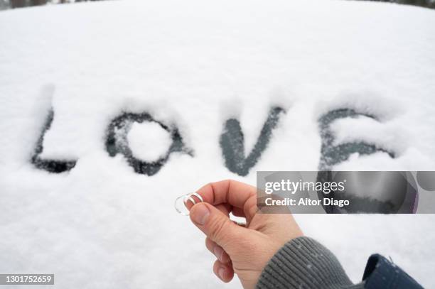 a person (man) holds two wedding rings right in front of the word love written on the snow. - frostbite fingers stock-fotos und bilder