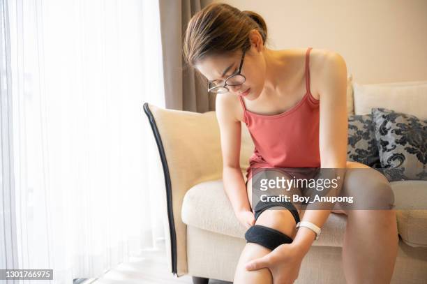 asian woman holding her knee while she having suffering from knee pain and she wearing knee braces for supports to be worn when you have pain in your knee. - knee length stock pictures, royalty-free photos & images