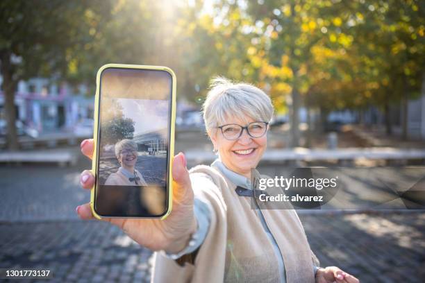 schöne seniorin zeigt ihr selfie - photo call stock-fotos und bilder
