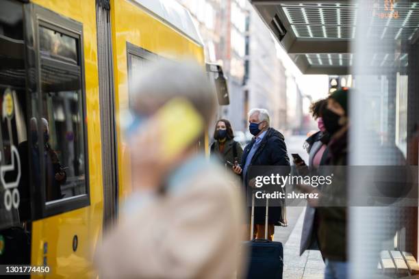 pendlergruppe in gesichtsmasken an straßenbahnhaltestelle - öffentliches verkehrsmittel stock-fotos und bilder