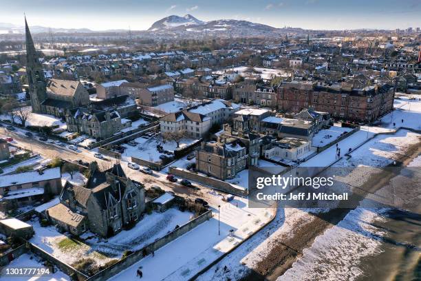 An aerial view of members of the public walking along a snow covered promenade at Portobello beach on February 12, 2021 in Edinburgh, Scotland. Heavy...