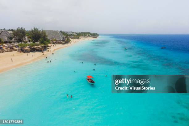scenic aerial view of the beautiful beach with turquoise colored ocean, red boat, hotels and group of swimming tourists on zanzibar island, tanzania - ilha de zanzibar imagens e fotografias de stock