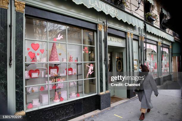 Woman wearing a protective face mask walks past the window of the Laduree pastry decorated with red hearts and boxes of macaroons before Valentine's...