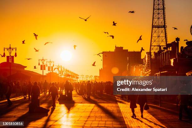 crowd of people walking on boardwalk in coney island, brooklyn during sunset, new york city, usa - street sunset stock pictures, royalty-free photos & images