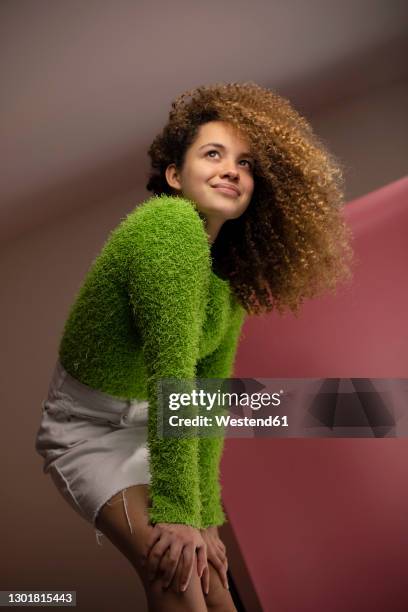 smiling young woman looking away while bending with hands on knees at studio - standing with hands on knees imagens e fotografias de stock