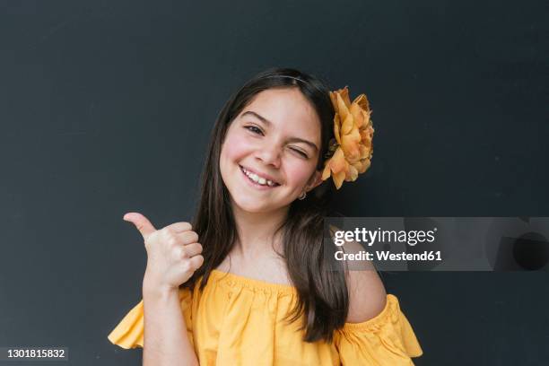 close-up of smiling girl wearing headband showing thumbs up against black background - black thumbs up white background stock pictures, royalty-free photos & images