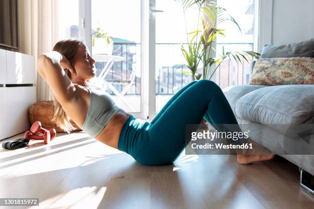 young woman doing sit-ups while exercising at home - curfew stock-fotos und bilder