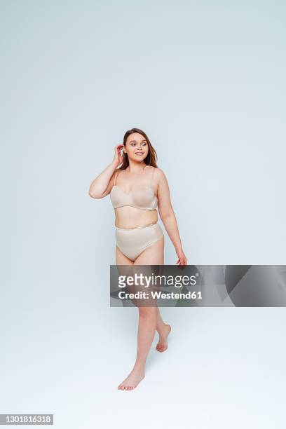 young woman in lingerie looking away while walking against white background - body photos et images de collection