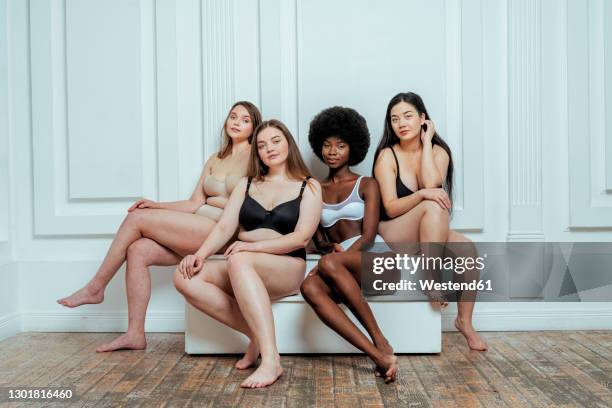 confident multi-ethnic group of models in lingerie  sitting against white wall - body types stock-fotos und bilder