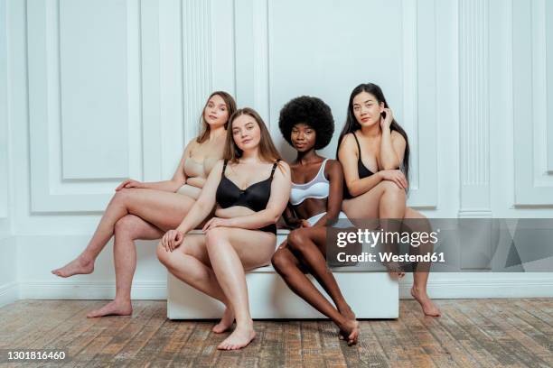 confident multi-ethnic group of models in lingerie sitting against white wall - les dessous stock-fotos und bilder