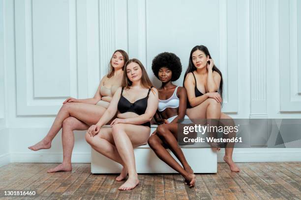 confident multi-ethnic group of models in lingerie  sitting against white wall - body photos et images de collection