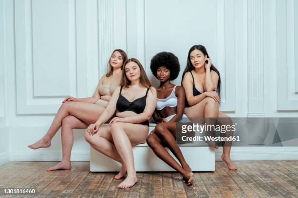 confident multi-ethnic group of models in lingerie  sitting against white wall - plus size fashion model stock pictures, royalty-free photos & images