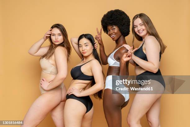 confident young women in lingerie standing against yellow background - voluptuous ladies photos et images de collection