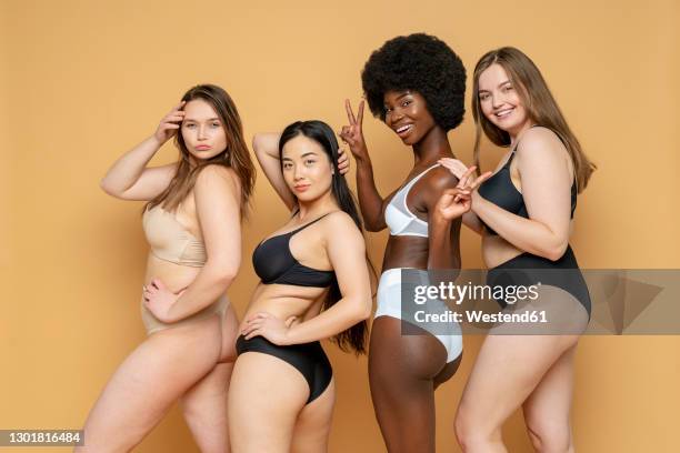 confident young women in lingerie standing against yellow background - chesty love stock pictures, royalty-free photos & images