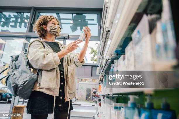 female customer wearing protective face mask while checking medicine in chemist store - pharmacy mask stock pictures, royalty-free photos & images